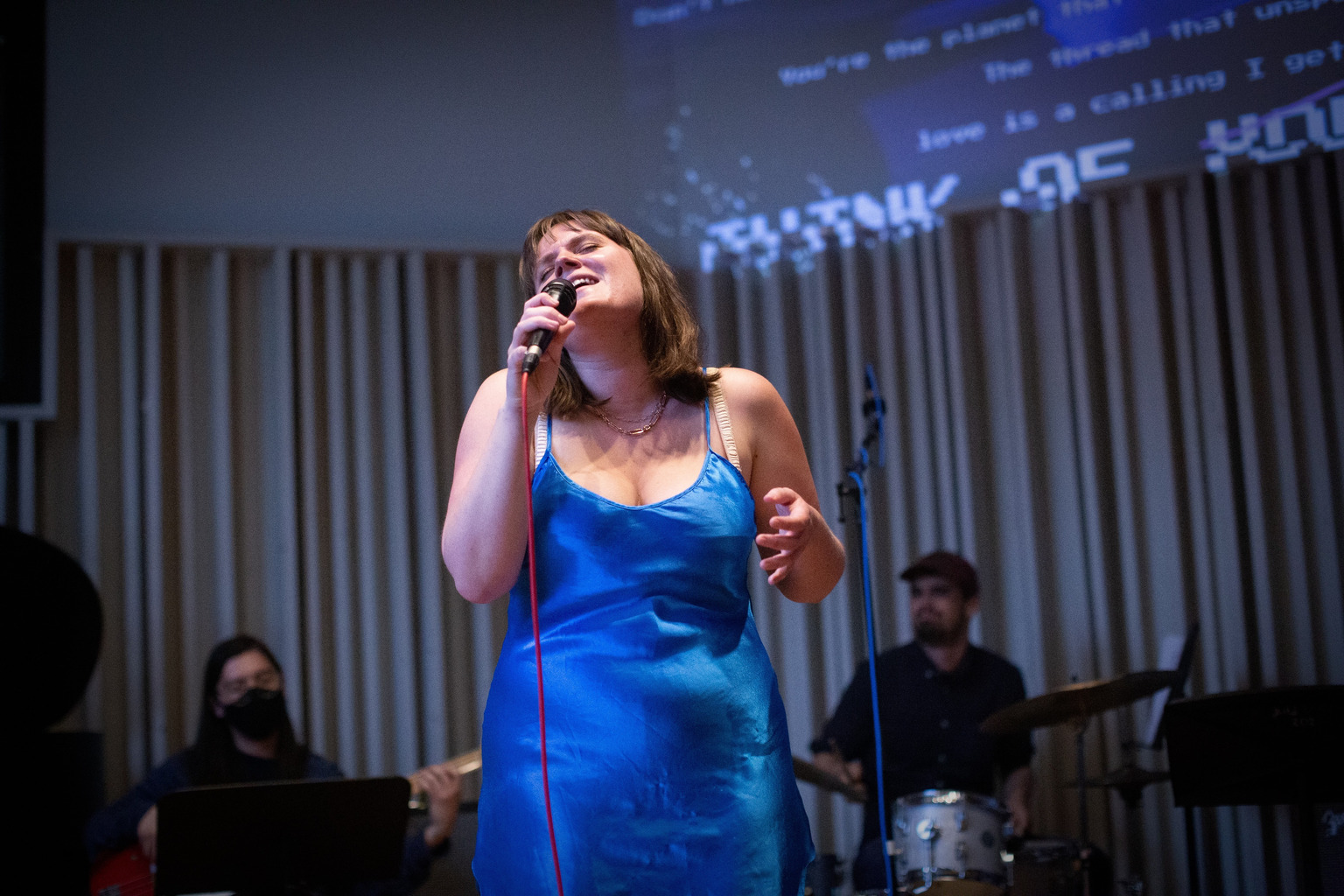 Madeline is singing with her eyes closed in front of a band at Bard College.