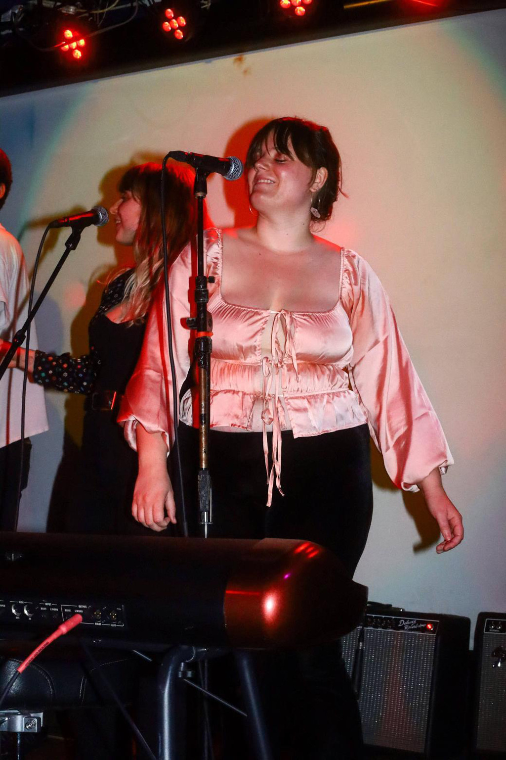 Madeline is singing with someone else on stage. The photo is taken with flash, and there is a curious shining effect with Madeline's pink velvet blouse and the red overhead lights.