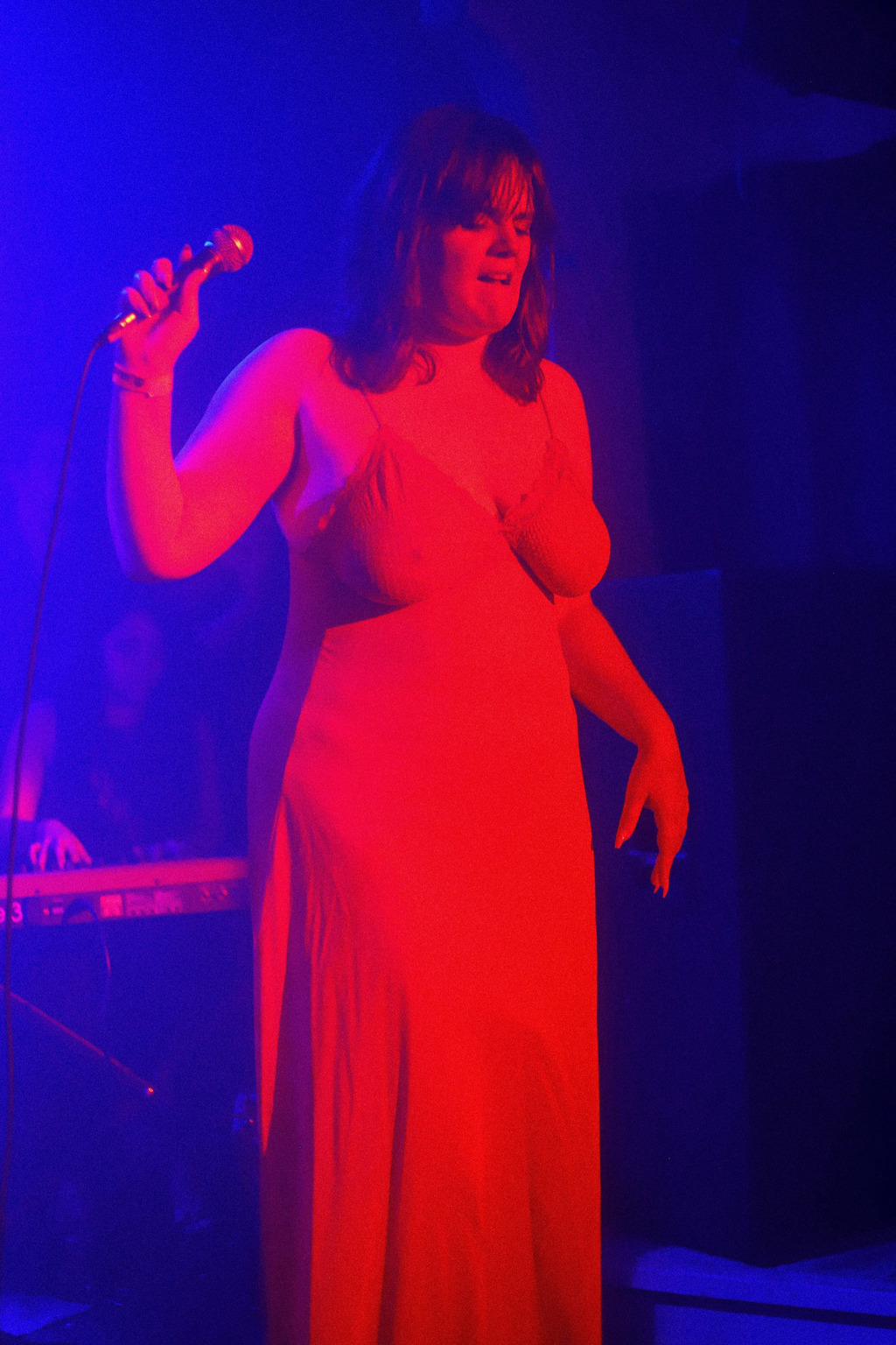 Madeline is standing on stage. The backlight is blue, but the spotlight is so red that the image almost appears duotone.