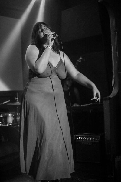 A black and white photo of Madeline, singing on stage with closed eyes.