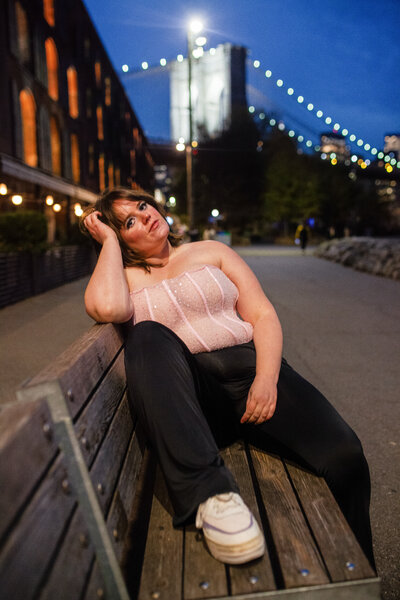 Madeline lounges on a public bench at twilight, one leg resting atop the steat.